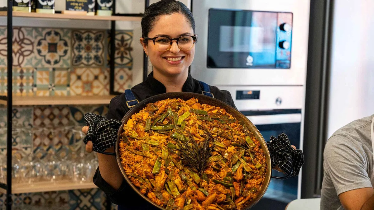Participants stirring a wide paella pan in a bright teaching kitchen, Spanish cooking workshop with paella and sangria in Málaga