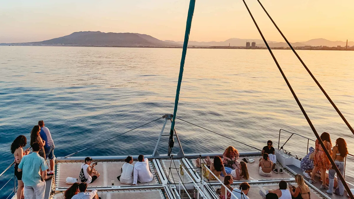Sailing catamaran leaving Malaga port at sunset on a bay cruise from Muelle Uno