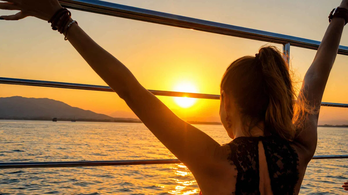 Passengers on the deck of a catamaran watching the sun set over the Malaga skyline