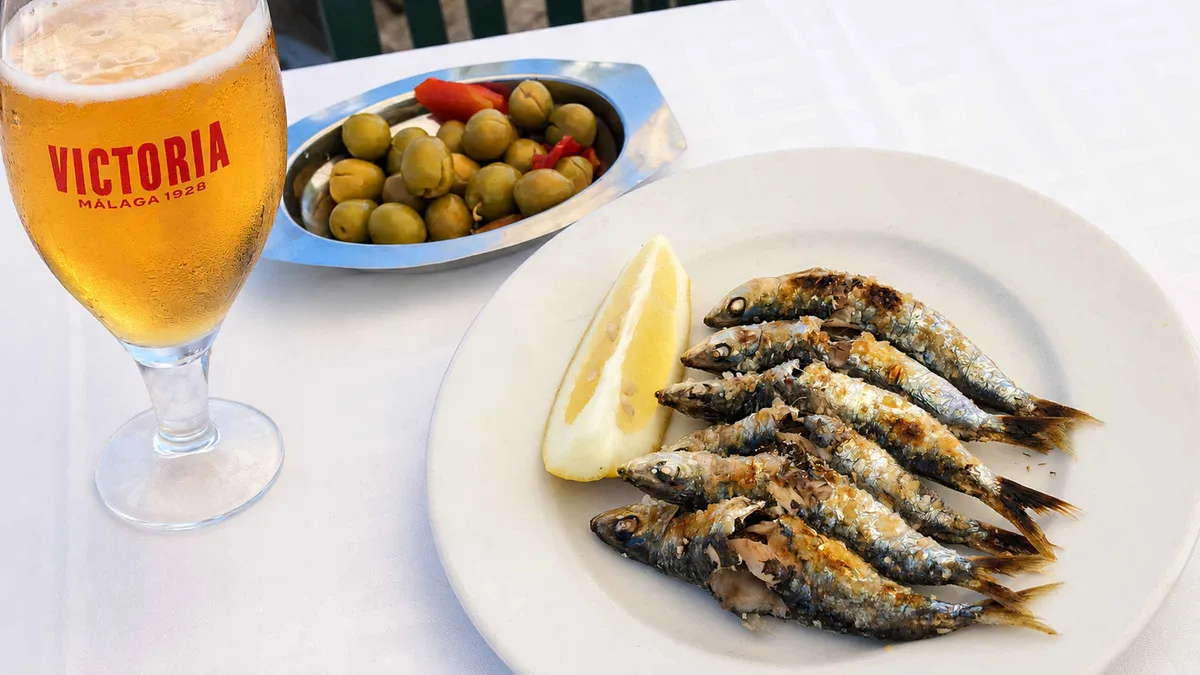 Sardines grilling on a cane over embers at a beach chiringuito in El Palo, Malaga
