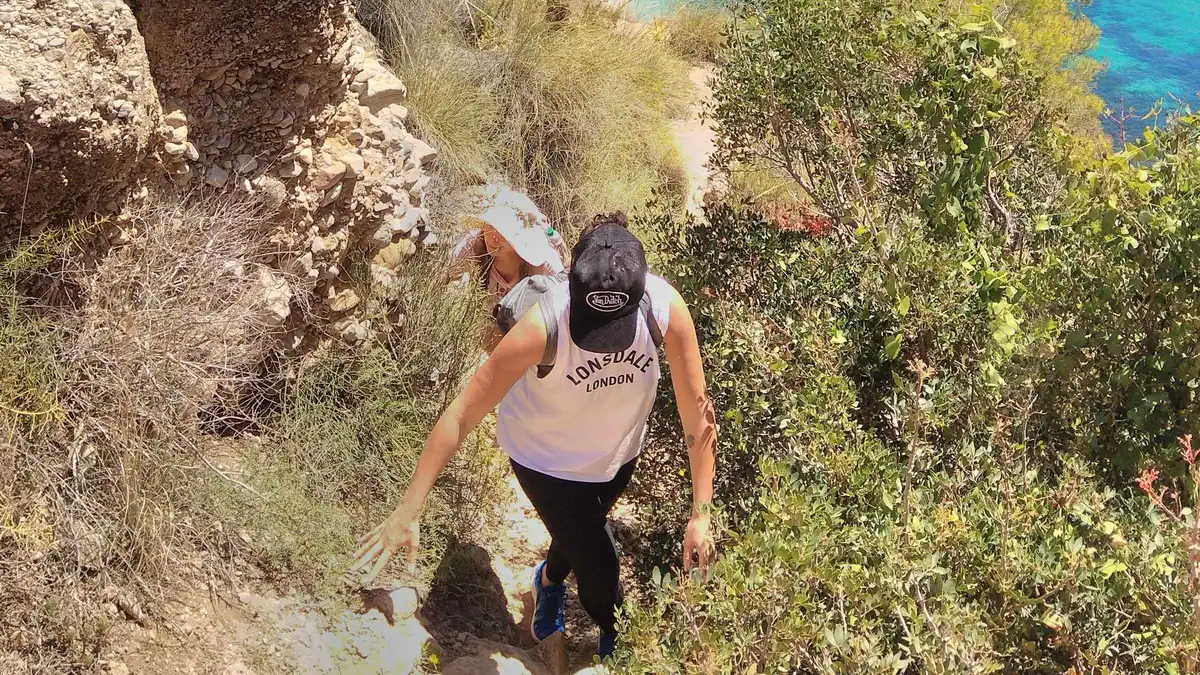 Hikers descending a narrow cliff path to a hidden cove on a Cliffs of Maro hike and snorkel trip from Málaga